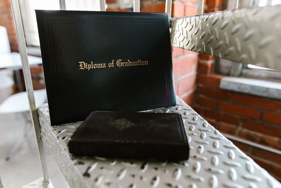 Close-up of a diploma and book on a metal staircase indoors, symbolizing academic achievement.